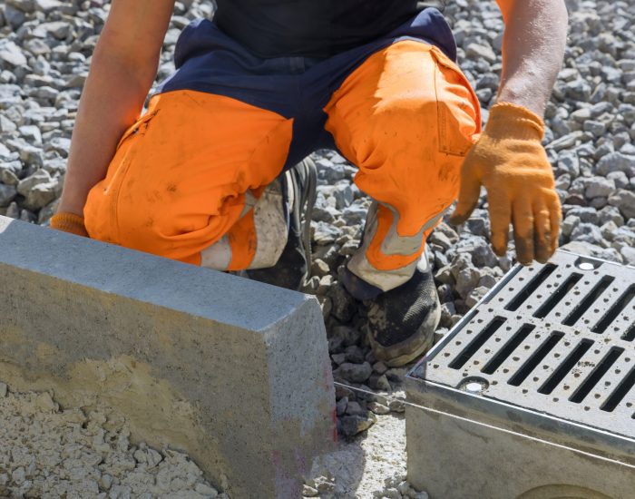 Municipal worker laying water drainage construction on well concrete with grate on well